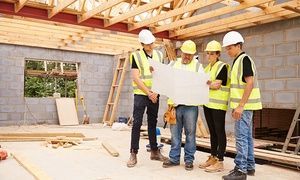 Builder On Building Site Looking At Plans With Apprentices